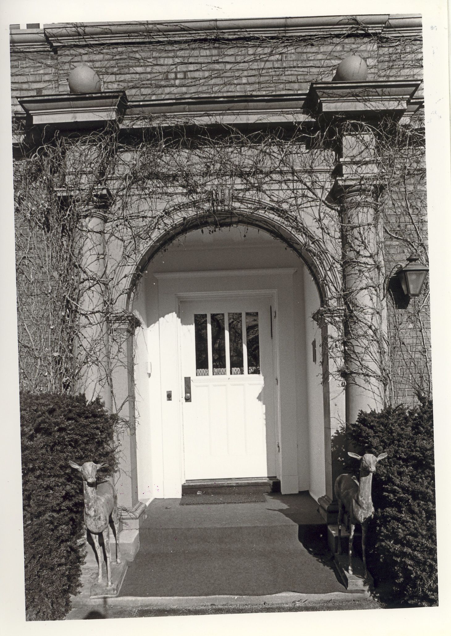 Arched and pillared entrance to residence, flanked by deer statues.