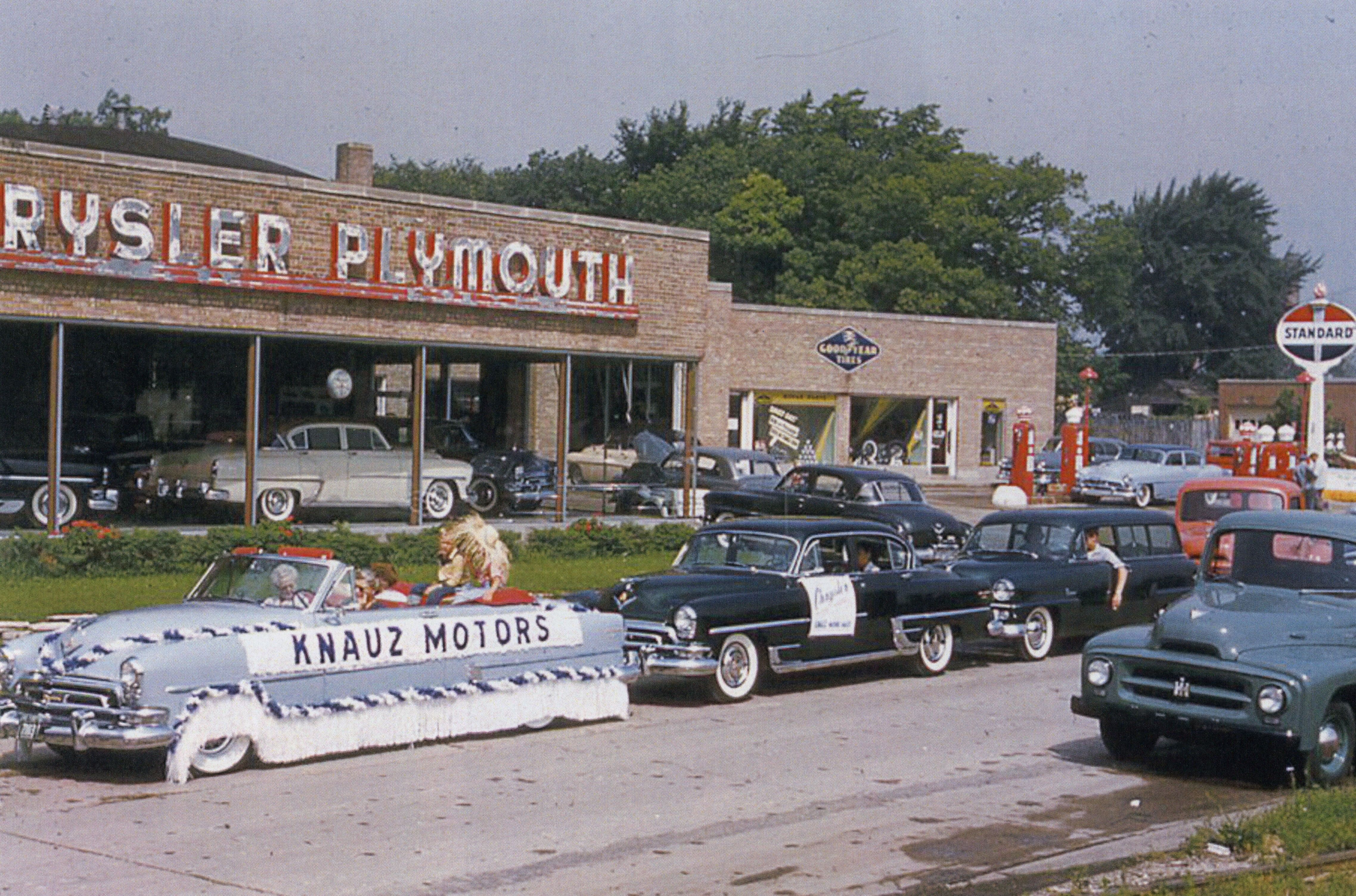 The Knauz Motors float and caravan of cars and trucks in the 1957 Lake Forest Day parade. Emmy Knauz is driving the pace car and her grandchildren are in the backseat.